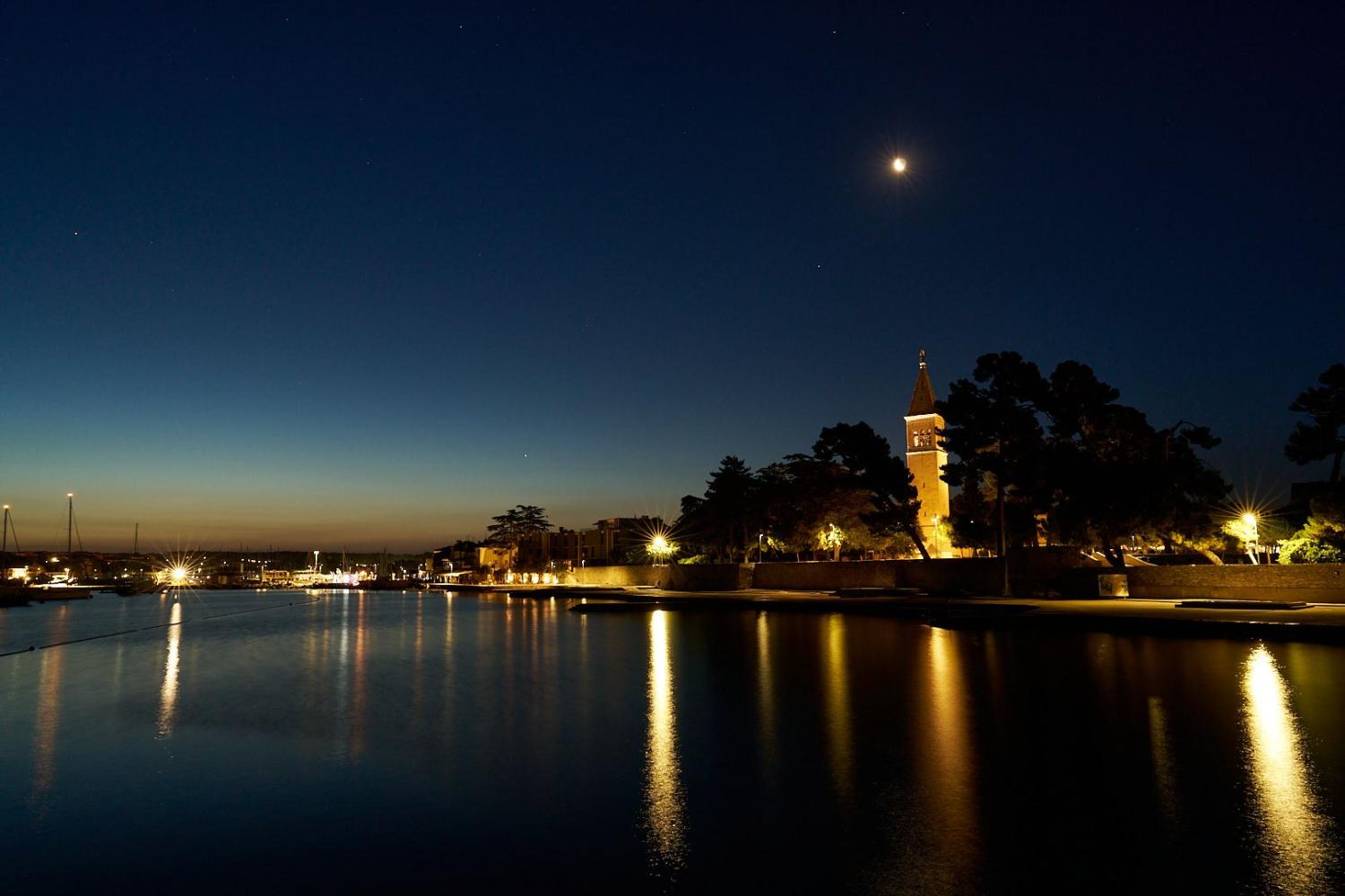 Aufnahme des Mondes über der Kirche St. Pelagius, der das Meer im Hafenbecken von Novigrad beleuchtet.